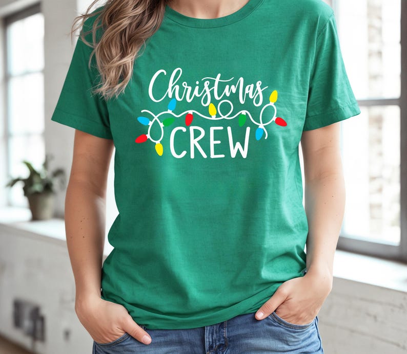 Puede incluir: Una camiseta verde con la frase "Christmas CREW" en blanco y una cadena de luces navide&ntilde;as de colores. La camiseta es de cuello redondo y la lleva una persona. Ideal para Navidad.