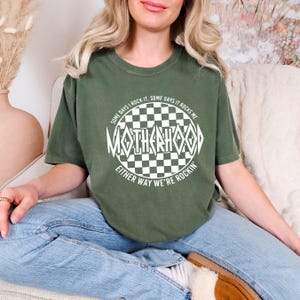 May include: Green t-shirt with a white checkered circle graphic and the text "SOME DAYS I ROCK IT. SOME DAYS IT ROCKS ME. MOTHERHOOD. EITHER WAY WE'RE ROCKIN'"