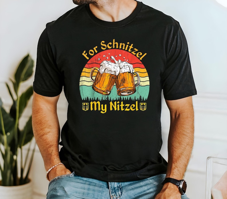 K&ouml;nnte beinhalten: Schwarzes T-Shirt mit einer Grafik im Vintage-Stil von zwei Bierkr&uuml;gen, die ansto&szlig;en, einem Sonnenuntergangs-Hintergrund und dem Text "For Schnitzel My Nitzel".