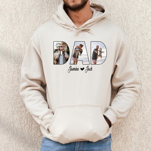 May include: A beige hoodie with the word "DAD" spelled out in large letters. Each letter is filled with a photo of a man with his children. The text "Jasmine &hearts; Jack" is printed below the word "DAD".