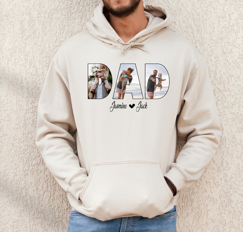 May include: A beige hoodie with the word "DAD" spelled out in large letters. Each letter is filled with a photo of a man with his children. The text "Jasmine &hearts; Jack" is printed below the word "DAD".