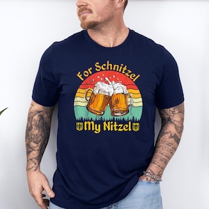 K&ouml;nnte beinhalten: Ein marineblaues T-Shirt mit einer Grafik im Vintage-Stil von zwei Bierkr&uuml;gen, die ansto&szlig;en, einem Sonnenuntergangs-Hintergrund und dem Text "For Schnitzel My Nitzel".