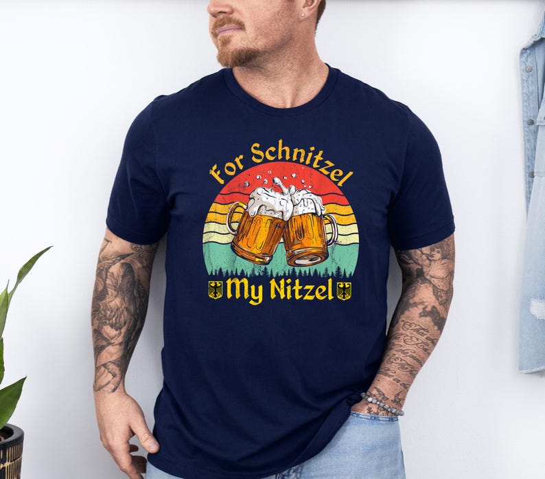 K&ouml;nnte beinhalten: Ein marineblaues T-Shirt mit einer Grafik im Vintage-Stil von zwei Bierkr&uuml;gen, die ansto&szlig;en, einem Sonnenuntergangs-Hintergrund und dem Text "For Schnitzel My Nitzel".