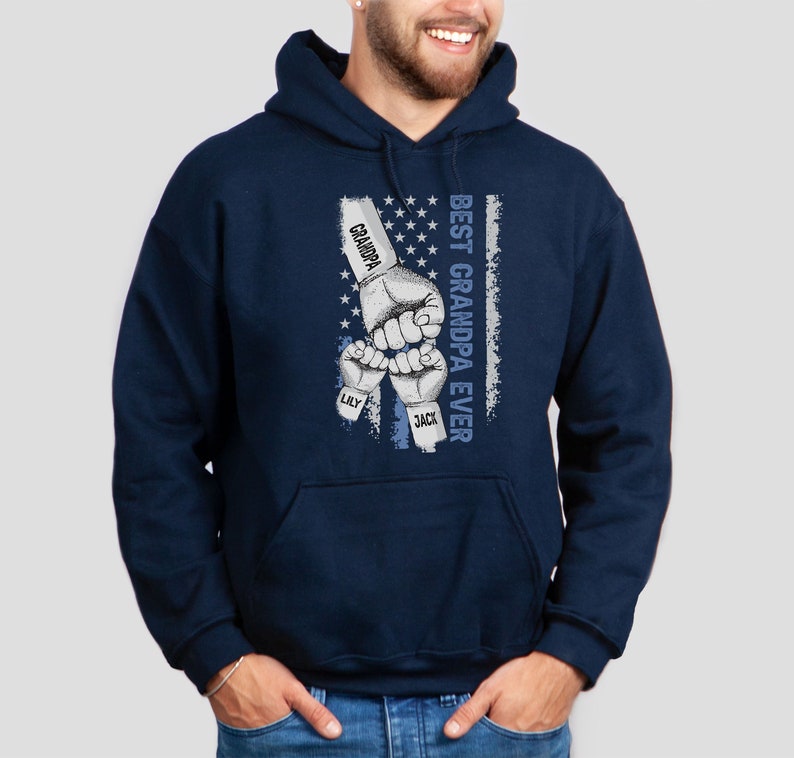 May include: Navy blue hooded sweatshirt with a graphic of three fists bumping each other. The fists have the names "Grandpa", "Lily", and "Jack" written on them. The graphic is set against a faded American flag background with the text "Best Grandpa Ever" written vertically.
