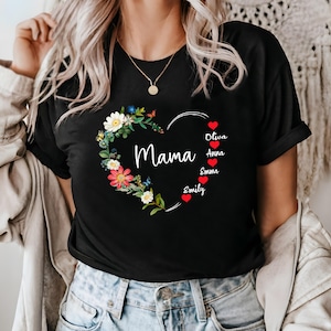 May include: Black t-shirt featuring a heart-shaped floral design with the word "Mama" in white script. The heart is adorned with colorful flowers and butterflies. Names are listed below the heart with red heart icons.