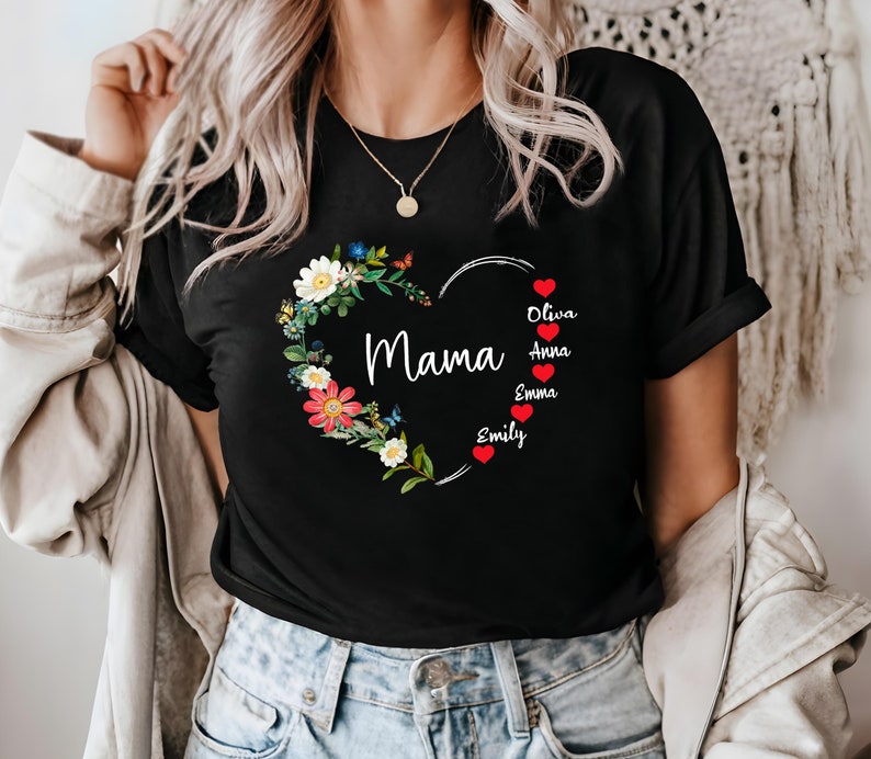 May include: Black t-shirt featuring a heart-shaped floral design with the word "Mama" in white script. The heart is adorned with colorful flowers and butterflies. Names are listed below the heart with red heart icons.