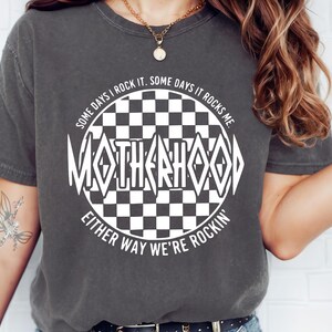 May include: A gray t-shirt with a white graphic design of a checkered circle with the text "SOME DAYS I ROCK IT. SOME DAYS IT ROCKS ME. MOTHERHOOD EITHER WAY WE'RE ROCKIN'"