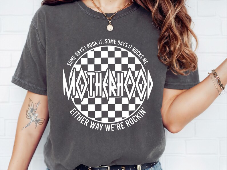 May include: A gray t-shirt with a white graphic design of a checkered circle with the text "SOME DAYS I ROCK IT. SOME DAYS IT ROCKS ME. MOTHERHOOD EITHER WAY WE'RE ROCKIN'"