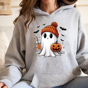 Pu&ograve; includere: Felpa con cappuccio grigia con grafica a tema Halloween. La grafica raffigura un fantasma amichevole con un berretto arancione, che tiene in mano una zucca e una bevanda. Pipistrelli neri e stelle sono sparsi intorno al fantasma.
