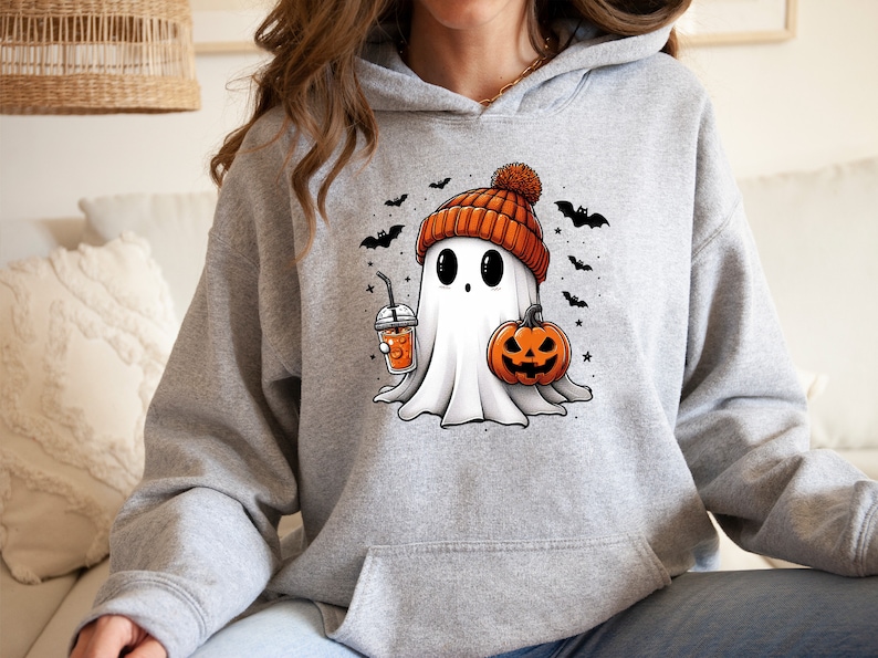 Pu&ograve; includere: Felpa con cappuccio grigia con grafica a tema Halloween. La grafica raffigura un fantasma amichevole con un berretto arancione, che tiene in mano una zucca e una bevanda. Pipistrelli neri e stelle sono sparsi intorno al fantasma.