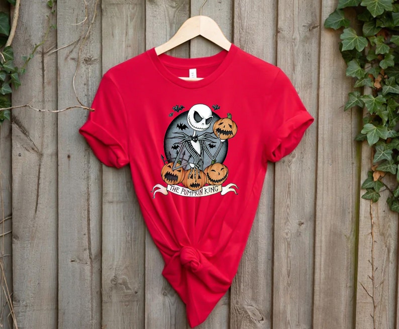 May include: A red t-shirt featuring a graphic of Jack Skellington from The Nightmare Before Christmas. The design includes Jack holding a pumpkin, surrounded by other pumpkins, with the text "THE PUMPKIN KING" on a banner.