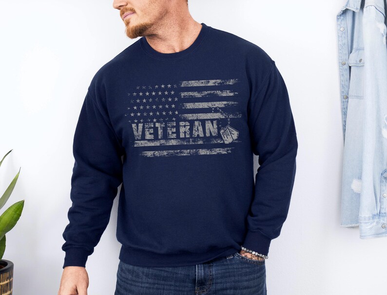 Peut inclure: Sweat-shirt bleu marine avec un motif de drapeau am&eacute;ricain vieilli et le mot "Veteran" en blanc.