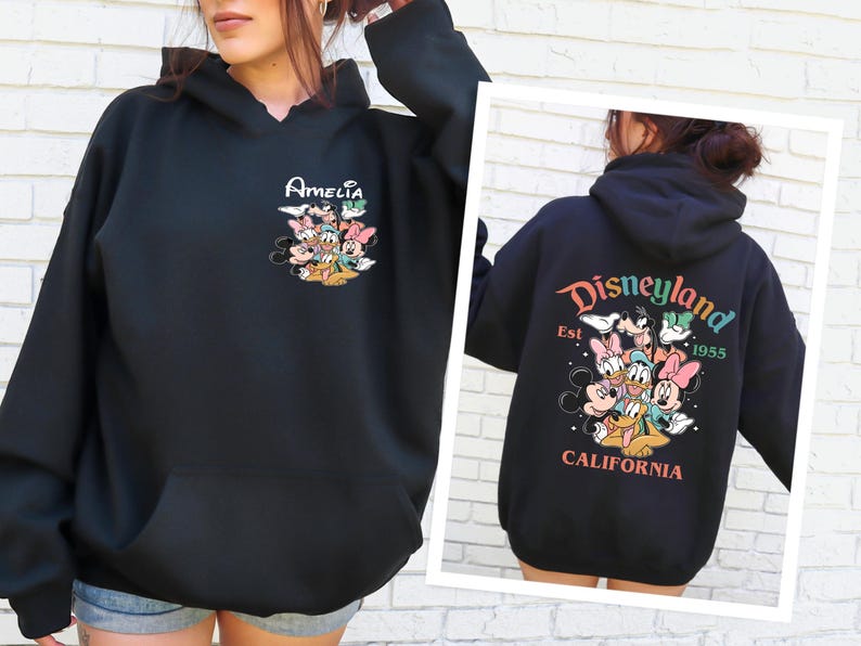 May include: Black hooded sweatshirt with a graphic of Mickey Mouse and friends. The text "Amelia" is printed on the front of the sweatshirt. The back of the sweatshirt has a graphic of Mickey Mouse and friends with the text "Disneyland Est. 1955 California".