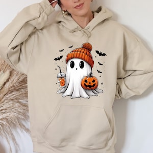 Pu&ograve; includere: Felpa con cappuccio beige con un fantasma dei cartoni animati con un berretto arancione, che tiene in mano una zucca e una bevanda. Pipistrelli e stelle nere circondano il fantasma. Perfetto per Halloween.