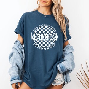 May include: A navy blue t-shirt with a white checkered circle graphic that says "Some days I rock it. Some days it rocks me. Either way we're rockin'." The text inside the circle says "Motherhood".