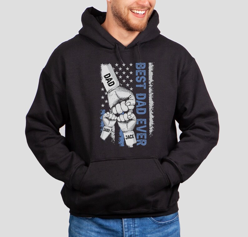 May include: Black hooded sweatshirt with a graphic of three fists raised in the air, with the words "Best Dad Ever" and the names "Dad", "Sander", and "Jack" printed on the fists. The graphic is set against a blue and white American flag background.
