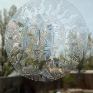 May include: A clear glass sun with a rainbow iridescent finish. The sun has a face with closed eyes and a stylized sunburst design.