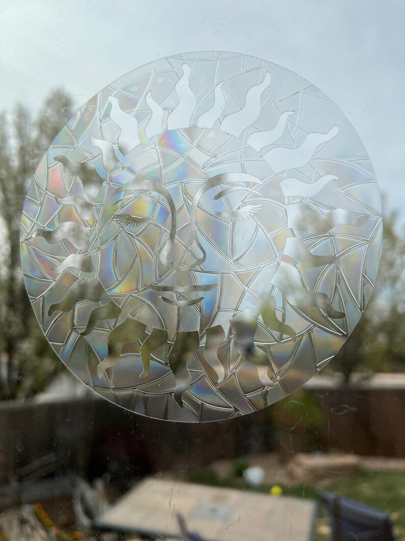May include: A clear glass sun with a rainbow iridescent finish. The sun has a face with closed eyes and a stylized sunburst design.