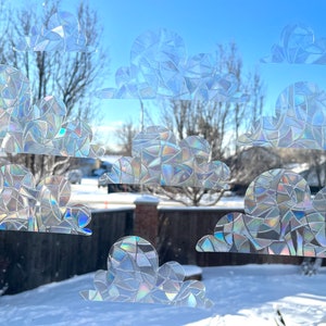 May include: A set of iridescent, rainbow-colored, cloud-shaped window clings. The clings are made of a textured, mosaic-like material and are designed to add a whimsical touch to any window.