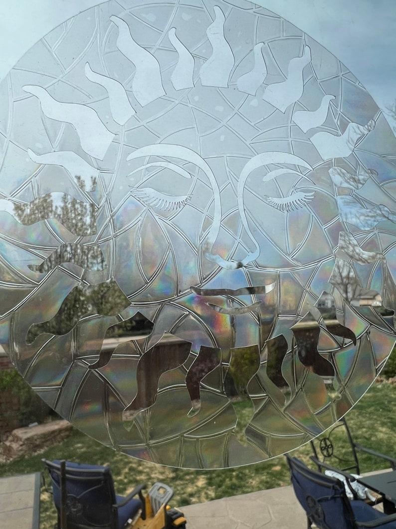 May include: A clear glass window with a decorative sun design etched into the surface. The sun has a face with closed eyes and a geometric pattern around it. The design is iridescent and reflects light.