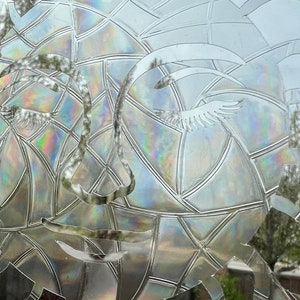May include: A close-up of a clear glass window with a decorative film applied. The film features a geometric pattern that creates the illusion of a face with eyelashes and a nose.