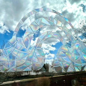 May include: A rainbow-shaped window cling with a iridescent, mosaic-like pattern. The cling is designed to look like a rainbow with clouds on either side.