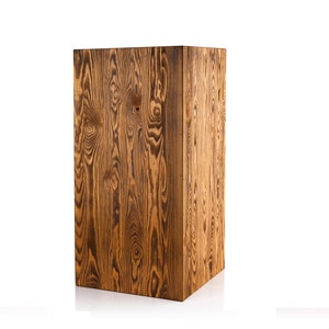 Puede incluir: Un pedestal de madera rectangular y alto con un acabado marr&oacute;n natural. La veta de la madera es visible y tiene un aspecto r&uacute;stico.