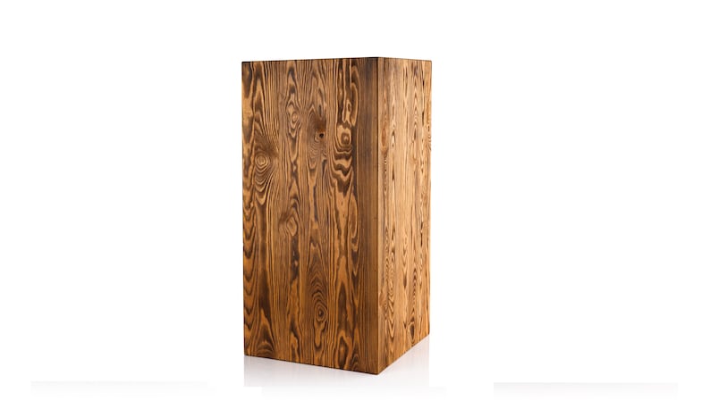 Puede incluir: Un pedestal de madera rectangular y alto con un acabado marr&oacute;n natural. La veta de la madera es visible y tiene un aspecto r&uacute;stico.