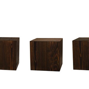 May include: Three dark brown wooden square blocks or cubes. The blocks are made of wood with a visible grain pattern.