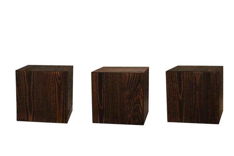 May include: Three dark brown wooden square blocks or cubes. The blocks are made of wood with a visible grain pattern.