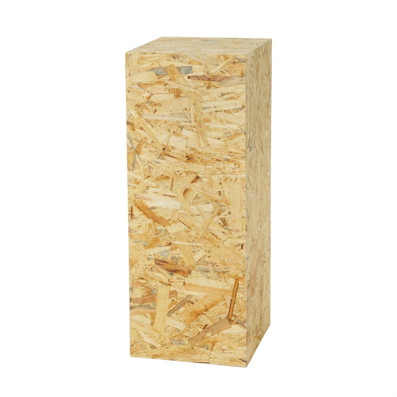 May include: A tall, rectangular wooden display stand made from oriented strand board (OSB). The stand is a light tan color with visible wood chips and grain, creating a textured surface. The stand is designed to be a pedestal for displaying items.