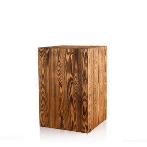 Puede incluir: Un taburete cuadrado de madera con un acabado de grano de madera marr&oacute;n oscuro. El taburete est&aacute; hecho de madera maciza y tiene un aspecto r&uacute;stico.