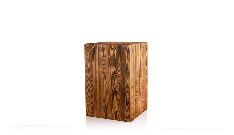 Puede incluir: Un taburete cuadrado de madera con un acabado de grano de madera marr&oacute;n oscuro. El taburete est&aacute; hecho de madera maciza y tiene un aspecto r&uacute;stico.