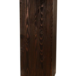 May include: A dark brown wooden pedestal with a smooth, rectangular top. The pedestal is made of natural wood with visible grain patterns.