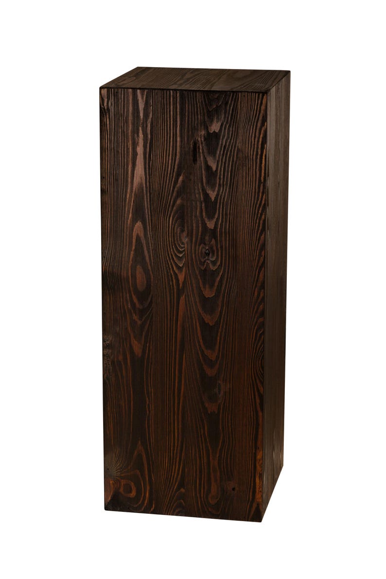 May include: A dark brown wooden pedestal with a smooth, rectangular top. The pedestal is made of natural wood with visible grain patterns.