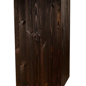 May include: A dark brown wooden cube, possibly a stool or a decorative piece. The wood grain is visible and the surface is smooth.