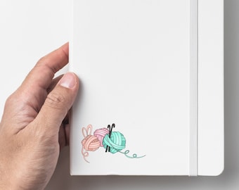 May include: White notebook with a spine and a small illustration of yarn balls and knitting needles in the bottom right corner.
