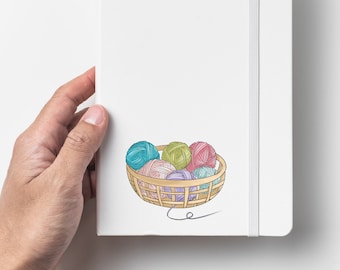 May include: A white notebook with a spine and a basket of colorful yarn balls. The yarn balls are in shades of blue, green, pink, and purple.