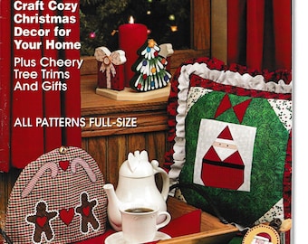 May include: The cover of "Crafting Traditions" magazine features Christmas decor. A red candle, Christmas tree, and gift-shaped ornaments sit on a wooden surface. A teapot, teacup, and a pillow with a Santa design are also visible. The magazine's title is in yellow.