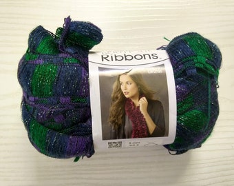 May include: A skein of Lion Brand "Ribbons" yarn in the color "LW2765". The yarn is a blend of green, purple, and blue with silver metallic threads. The yarn is shown on a white surface with a label that shows a woman wearing a scarf made from the yarn.