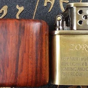 May include: A gold-colored lighter with a wooden case. The lighter has the word "ZORRO" engraved on the front and a safety warning printed below.