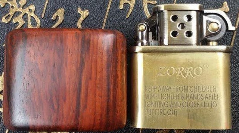 May include: A gold-colored lighter with a wooden case. The lighter has the word "ZORRO" engraved on the front and a safety warning printed below.