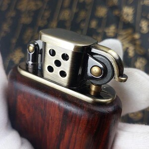 May include: A wooden lighter with a brass top and a black metal wick adjuster. The lighter has a dark wood grain pattern and a polished brass finish.