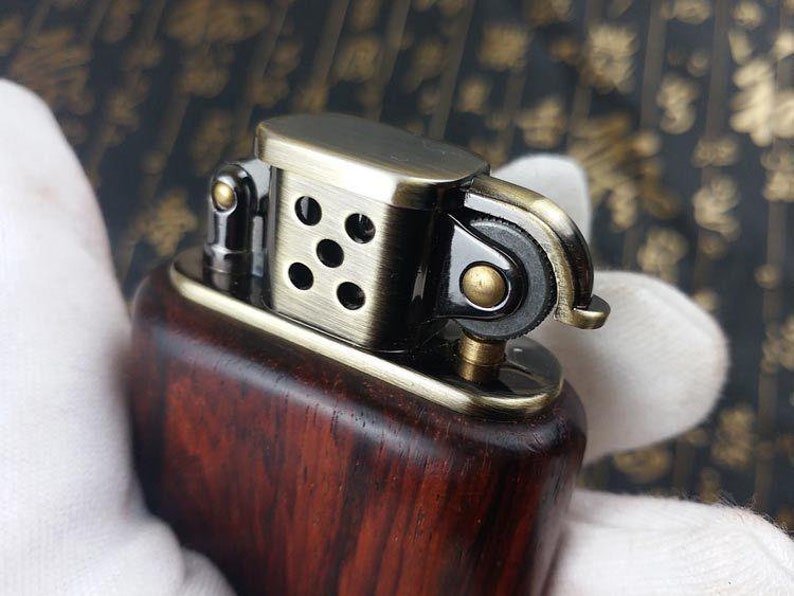 May include: A wooden lighter with a brass top and a black metal wick adjuster. The lighter has a dark wood grain pattern and a polished brass finish.