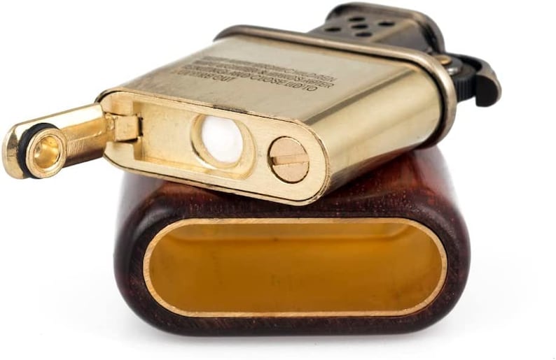 May include: A gold-toned lighter with a wooden case. The lighter has a wick and a flint, and the case has a dark brown wood grain.