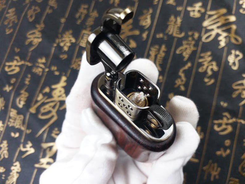 May include: A wooden and metal lighter with a silver and black finish. The lighter has a small, round, silver wick and a black, rectangular body.