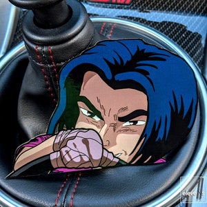 May include: A blue-haired anime character with a pink and black glove is holding a steering wheel. The character is looking to the right. The image is a sticker that is placed on a car's gear shift.