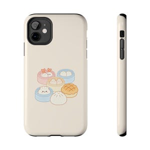 以下が含まれることがあります： パステルカラーの蒸し器に入った点心の漫画イラストが描かれた、クリーム色の携帯電話ケース。ケースは黒い縁取りと光沢のある仕上がりで、保護とキュートな美しさを提供します。