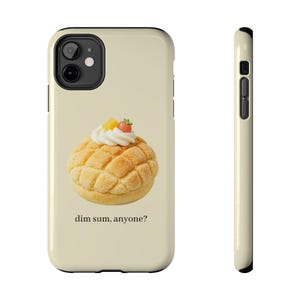 以下が含まれることがあります： ベージュ色のスマホケース。メロンパンのクローズアップ画像がプリントされています。ホイップクリーム、マンゴー、さくらんぼがトッピングされています。「dim sum, anyone?」の文字がパンの下に印刷されています。