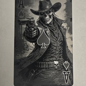 May include: Ace of Spades playing card featuring a skeletal cowboy in a hat, holding a gun. The card has a black and white design with the spade symbol and the letter "A" visible. The cowboy is wearing a long coat and a belt with a skull buckle.